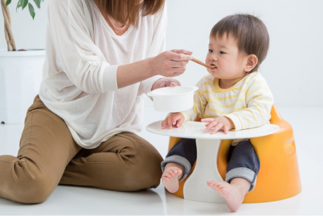 お子様を椅子に座らせて食事を与えるお母さん